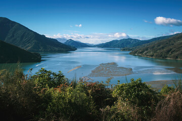 Obraz premium Tranquil landscape of Pelorus Sound in Marlborough Sounds, New Zealand, with blue tidal water, calm pacific ocean, distant mountains and valley, dramatic clouds on a clear sunny day