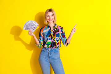 Photo portrait of lovely young lady hold money fan point empty space dressed stylish colorful garment isolated on yellow color background