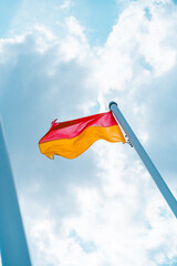 Bright Red and Yellow Flag Waving Against a Cloudy Blue Sky