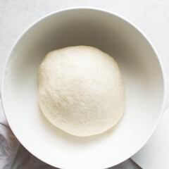 Overhead view of challah dough in a white mixing bowl, top view of homemade challah dough rising in a white mixing bowl, process of making challah
