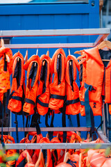 Bright Orange Life Jackets Hanging on a Rack Outside Near a Blue Wall