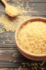 Rice grains on brown plate and spoon on brown wooden background