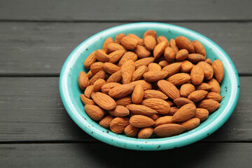Fresh natural healthy almonds nuts in blue plate on black wooden background.