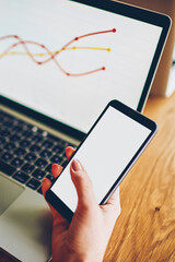 Cropped image of woman's hands typing on smartphone device with blank screen area and sharing multimedia files via bluetooth connection on laptop computer with wireless internet.Netbook with schemes