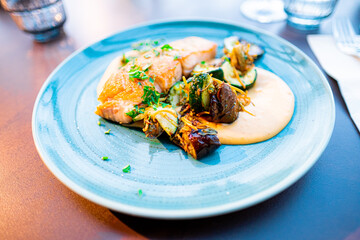 Delicious Plated Salmon Dish with Grilled Vegetables and Creamy Sauce Served on a Blue Plate in a Fine Dining Setting