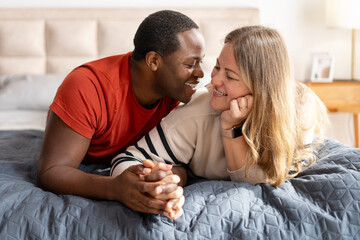 Happy lovely man and woman looking each other holding hands on bed at home