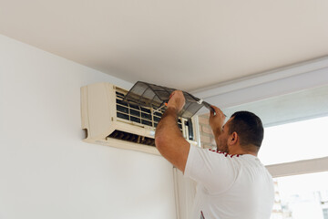 technician man taking out dirty filters from air conditioner in apartment