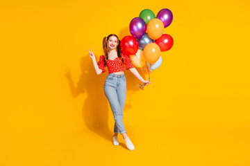 Fototapeta premium Full body photo of attractive young woman hold air balloons show v-sign dressed stylish red clothes isolated on yellow color background