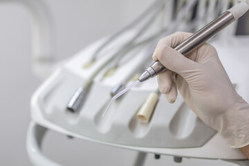Gloved hand holding a dental suction tool with multiple handpieces in the background of a clean, professional dental unit