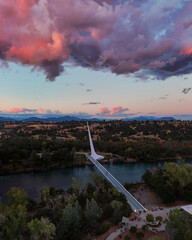 Stunning aerial view of the Sundial Bridge at dusk, with vibrant pink and purple clouds reflecting the fading light over the river and surrounding landscape.