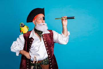Photo of senior funny pirate grandpa hold binoculars tube look empty space wear masquerade party...
