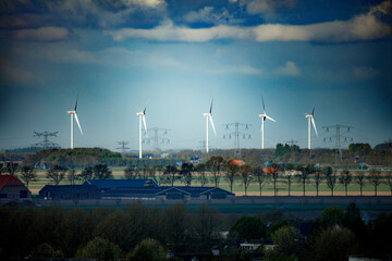 Obraz premium Panoramic view of Dutch countryside. Wind turbines, power lines, and farm buildings are prominent features. A mix of farmland and trees is visible.