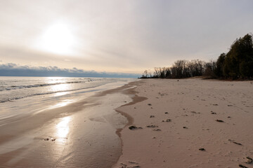 The morning sun appears behind the filtering clouds and reflects off Lake Michigan in early December at Harrington Beach State Park, Belgium, Wisconsin, the beach is frozen and silent