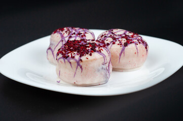 Three donuts are on a white plate on a black background. Donuts in white glaze decorated with pink sprinkles