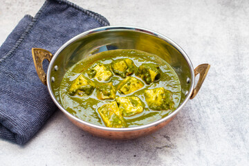 A bowl of palak paneer, an Indian dish with paneer cubes in spinach curry, on a textured grey surface.