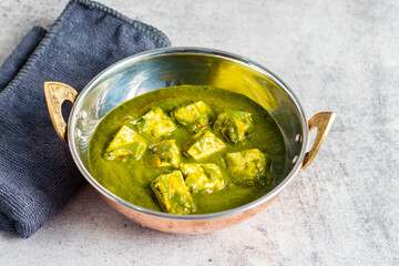 A bowl of palak paneer, an Indian dish with paneer cubes in spinach curry, on a textured grey surface.