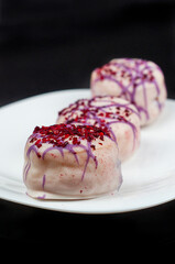 Sweet donuts in white glaze are decorated with pink powder on top. Three isolated  donuts are placed on a white plate on a black background