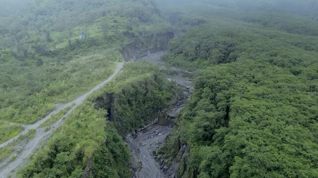 Aerial View of Dramatic Sand Mining Activity in Volcanic Lava Gorge Amid Foggy and Overcast Skies