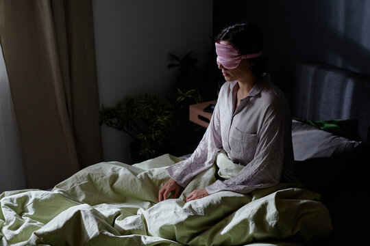 High angle shot of unrecognizable woman suffering from somnambulism sitting in bed at night