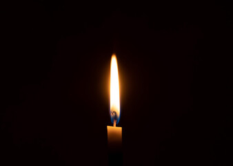 A single burning candle flame or light glowing on an orange candle on black or dark background on...