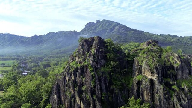 aerial view of ancient limestone rocky mountains, cliffs, and green trees with morning mist surrounded by rice fields. towering rocky hill of Sepikul mountain in Indonesia. 