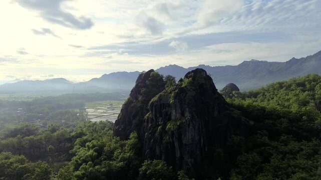 aerial view of ancient limestone rocky mountains, cliffs, and green trees with morning mist surrounded by rice fields. towering rocky hill of Sepikul mountain in Indonesia. 
