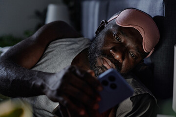 Medium close up of African American suffering from insomnia checking his social networks at night