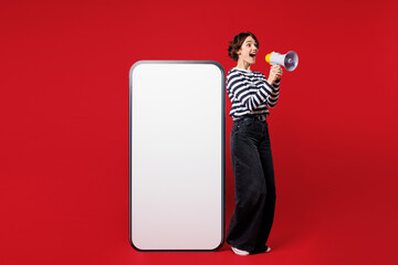 Full body young woman wear blue striped sweatshirt casual clothes big huge blank screen mobile cell phone smartphone with copy space mockup area scream in megaphone isolated on plain red background.
