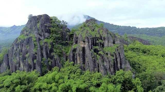 aerial view of ancient limestone rocky mountains, cliffs, and green trees with morning mist surrounded by rice fields. towering rocky hill of Sepikul mountain in Indonesia. 