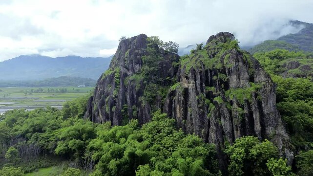 aerial view of ancient limestone rocky mountains, cliffs, and green trees with morning mist surrounded by rice fields. towering rocky hill of Sepikul mountain in Indonesia. 