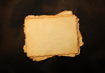 Close up stack of several blank old antique vintage brown paper parchment sheets with aged and weathered edges over dark table background