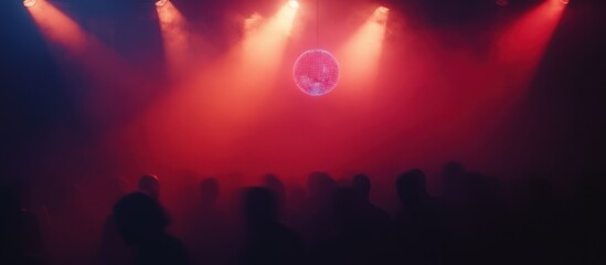 Red-lit silhouettes of a crowd at a concert with a disco ball.