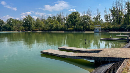 Obraz premium Scenic view of a calm lake surrounded by lush green trees under a clear blue sky, ideal for nature, relaxation, and eco-tourism concepts.