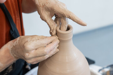Close-up of a potter's hands making a ceramic vase on a potter's wheel. 