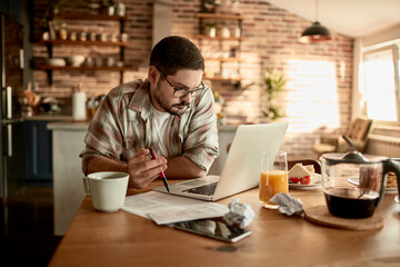 Man working on laptop at kitchen table in a cozy home setting