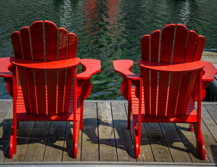 Two wooden adirondack red chairs on a wooden deck by lake Simcoe at Friday Harbour, Ontario, Canada