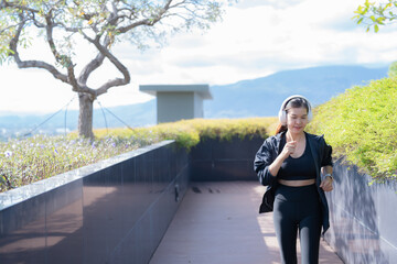 Young athletic woman jogging on rooftop walkway wearing sportswear and wireless headphones, enjoying her outdoor workout with mountains in background