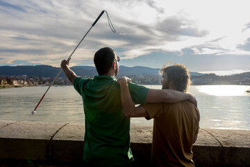 Blind man and supportive friend enjoying scenic waterfront view