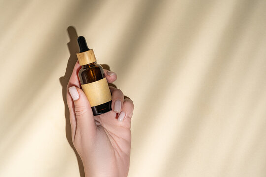Elegant cosmetic dropper bottle held in cropped anonymous hand