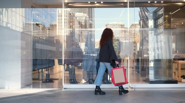 Young woman walks past modern storefront windows while carrying a shopping bag