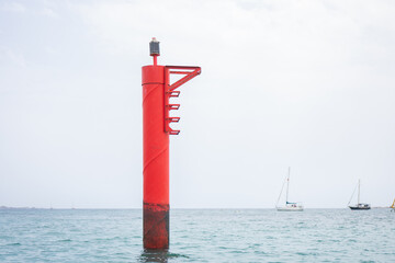 Red and white port marker buoy with sailboats in the distance