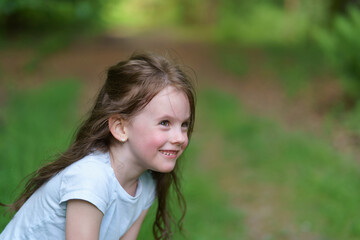 smiling girl in t-shirt and denim shorts on dirt path in summer forest. Concept of healthy cheerful active child