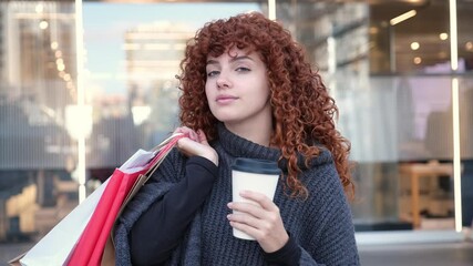 Redhead woman enjoys a coffee after shopping, carrying bags and smiling