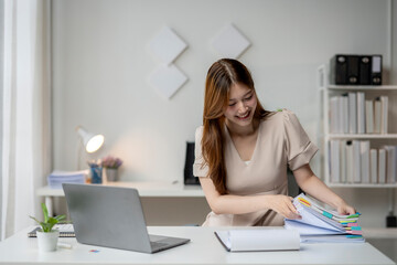 A woman is sitting at a desk with a laptop and a stack of papers
