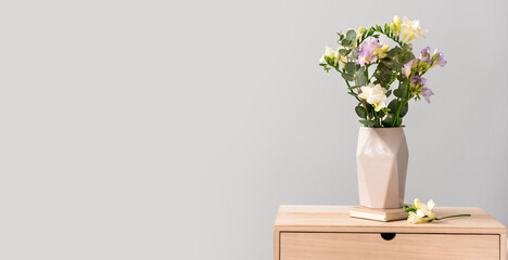 Vase with beautiful freesia flowers on table against light background