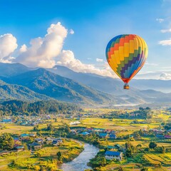 Fototapeta premium A colorful hot air balloon floats over a scenic landscape with mountains and a river.