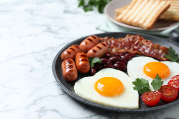Delicious breakfast with heart shaped fried eggs and  sausages on white marble table, closeup