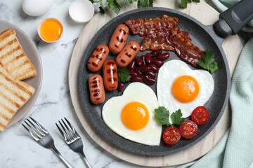 Delicious breakfast with heart shaped fried eggs and  sausages served on white marble table, flat lay