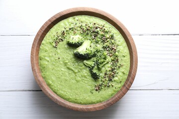 Delicious broccoli cream soup in bowl on white wooden table, top view