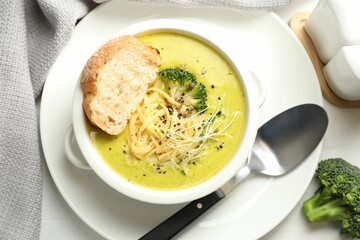 Delicious broccoli cream soup served on white table, flat lay